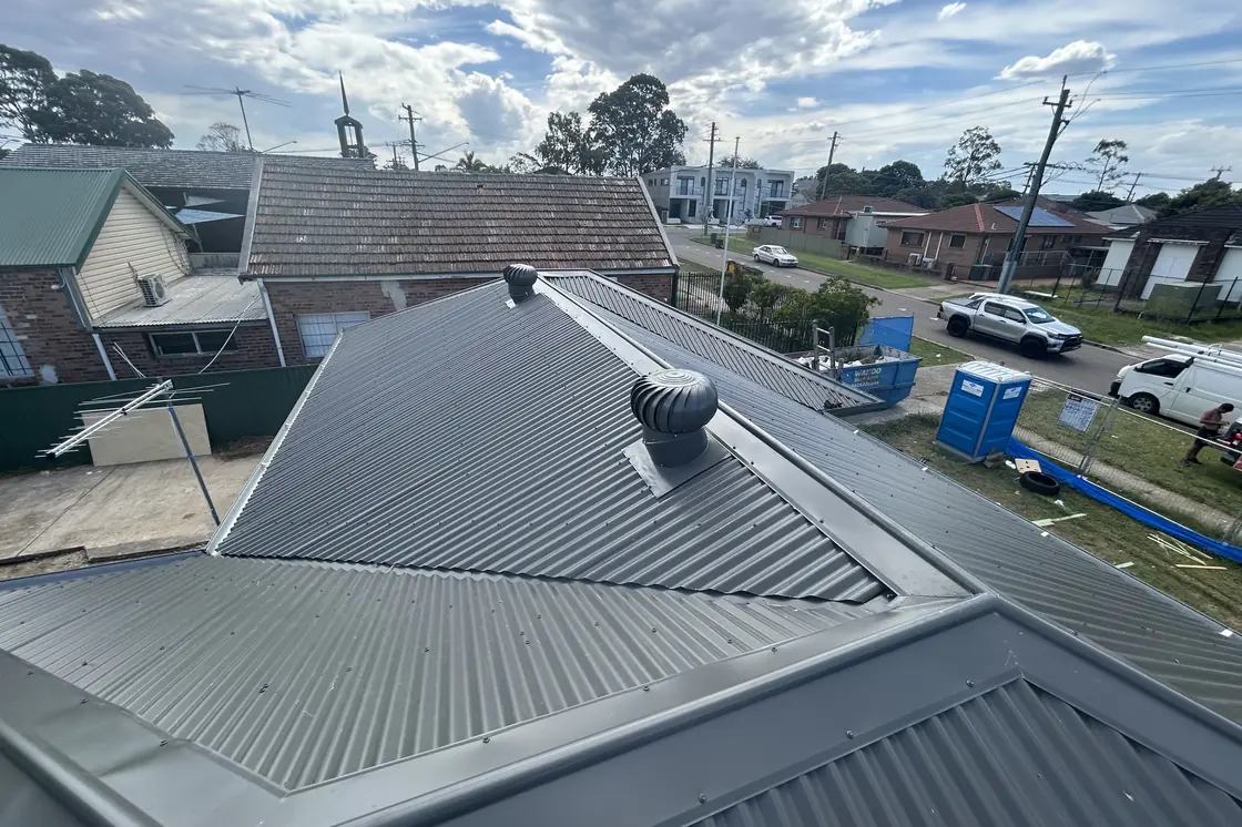 A new steel hip roof with a whirlybird, photographed out over a street of older tiled roofs