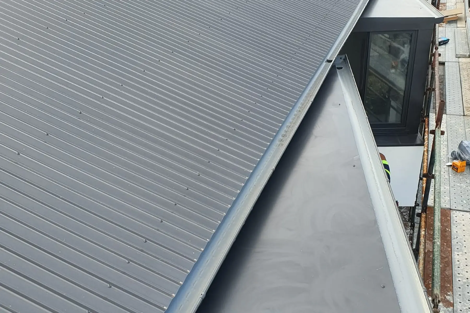 A long new roof plane finished into a fresh gutter, the wall of the building alongside