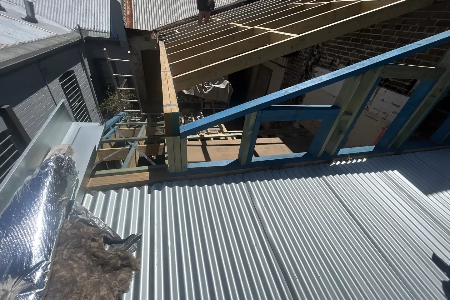 New sheeting going on over an exposed timber and steel frame, the structure still open beneath