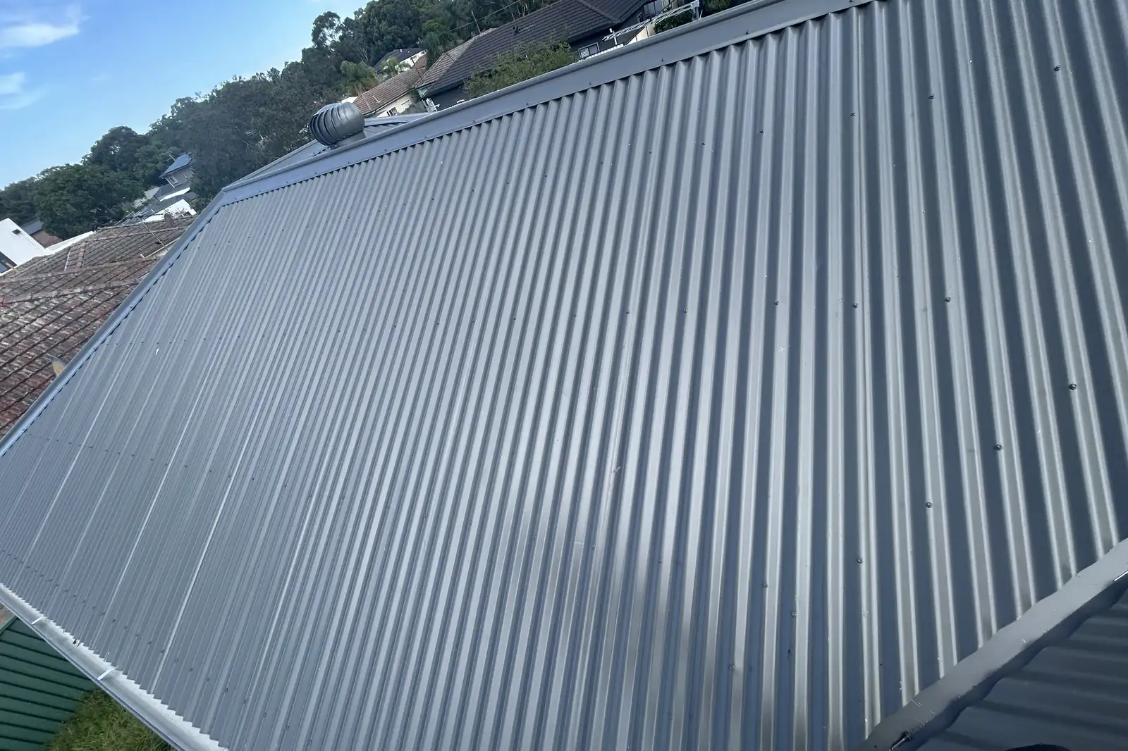 A wide plane of new steel sheeting across a single-storey roof, tiled neighbours either side