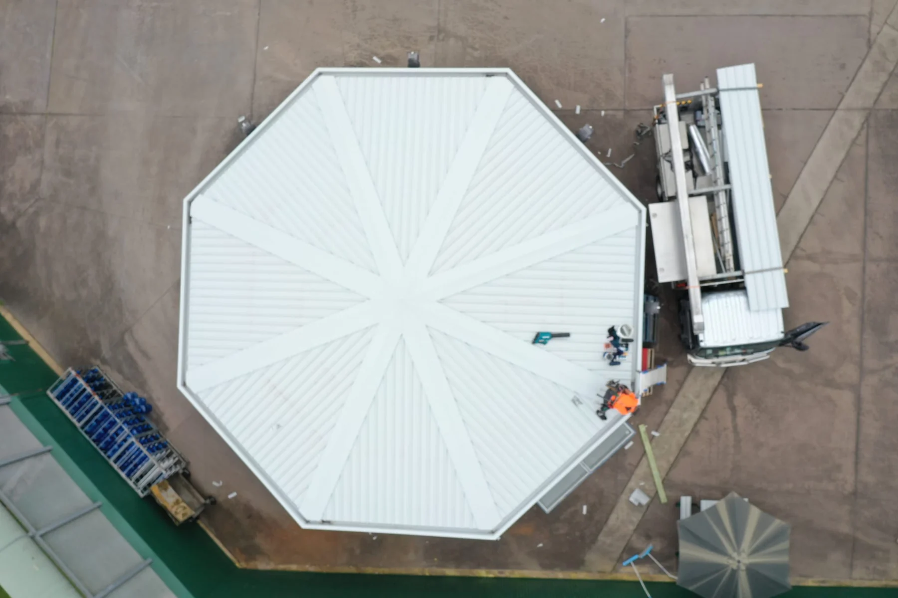 An octagonal roof in new white steel, photographed from directly above with materials stacked alongside