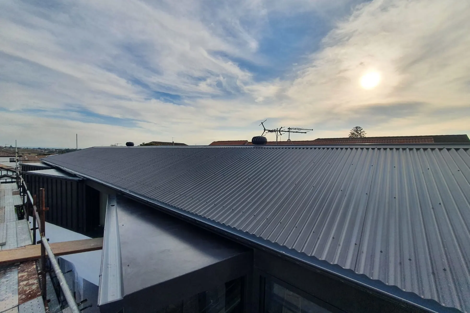 Low sun and high cloud over a dark low-pitched roof, aerials standing along the ridge
