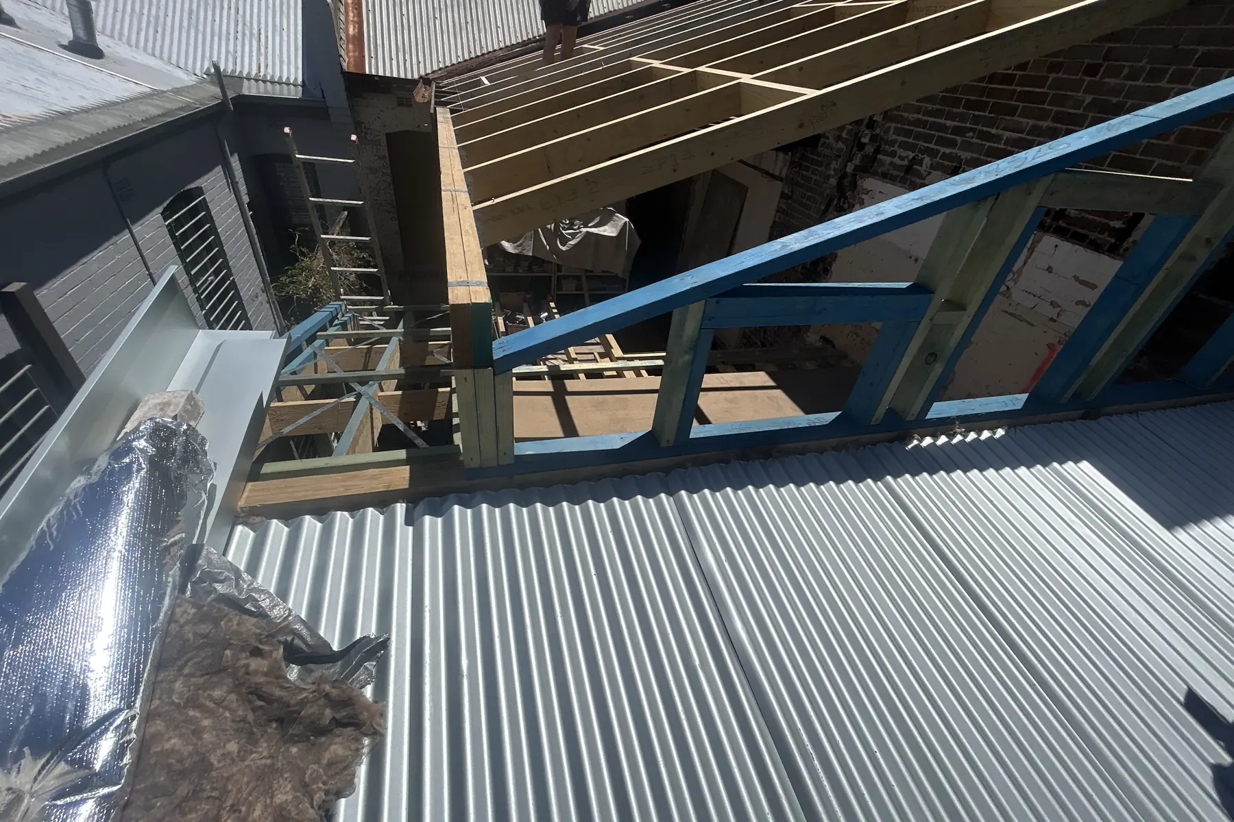 New sheeting going onto a light framed structure, with the painted steel frame and battens still exposed at the open end