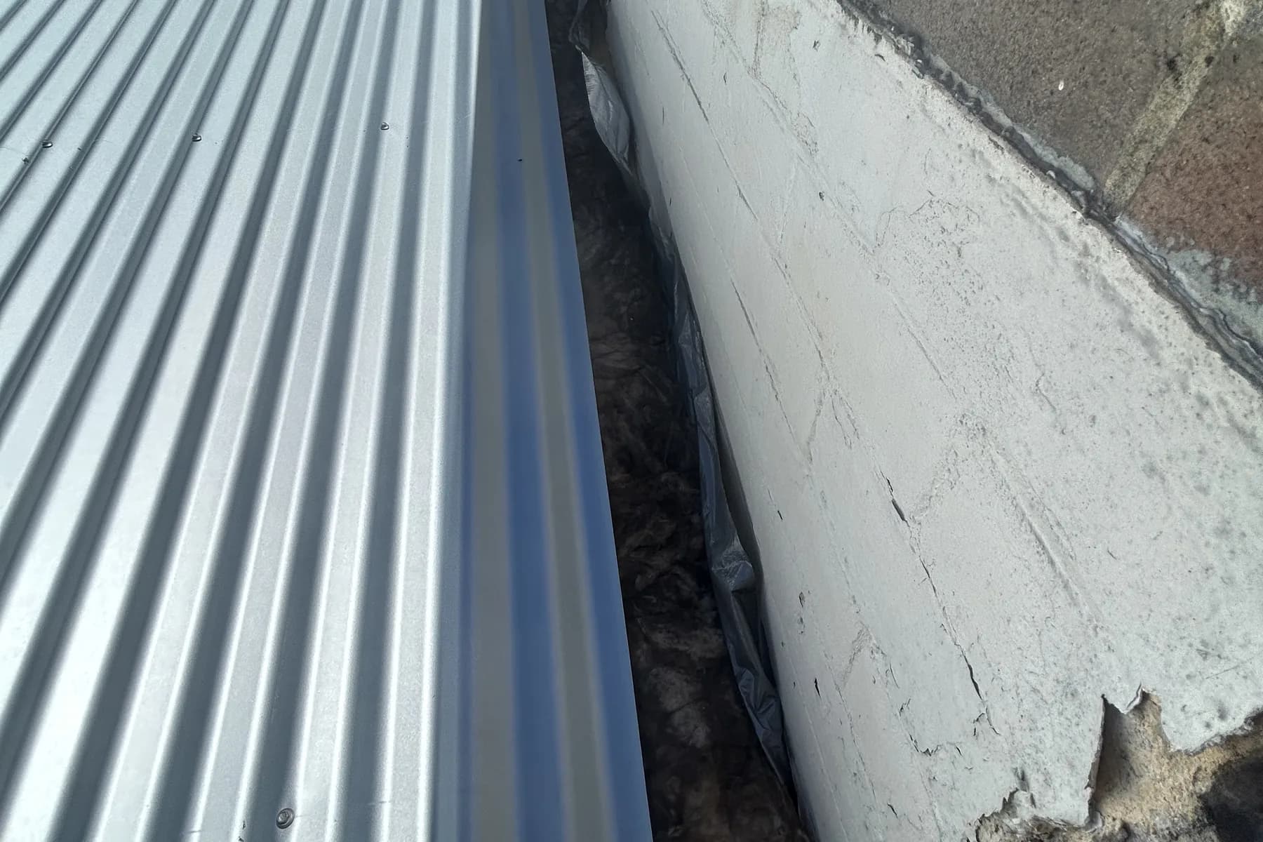 A new steel box gutter running between a metal roof and an old masonry wall
