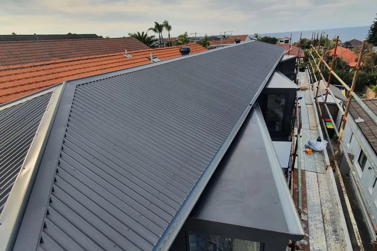 A new dark grey metal roof on a rebuilt house, still scaffolded, the ridge running out towards the water