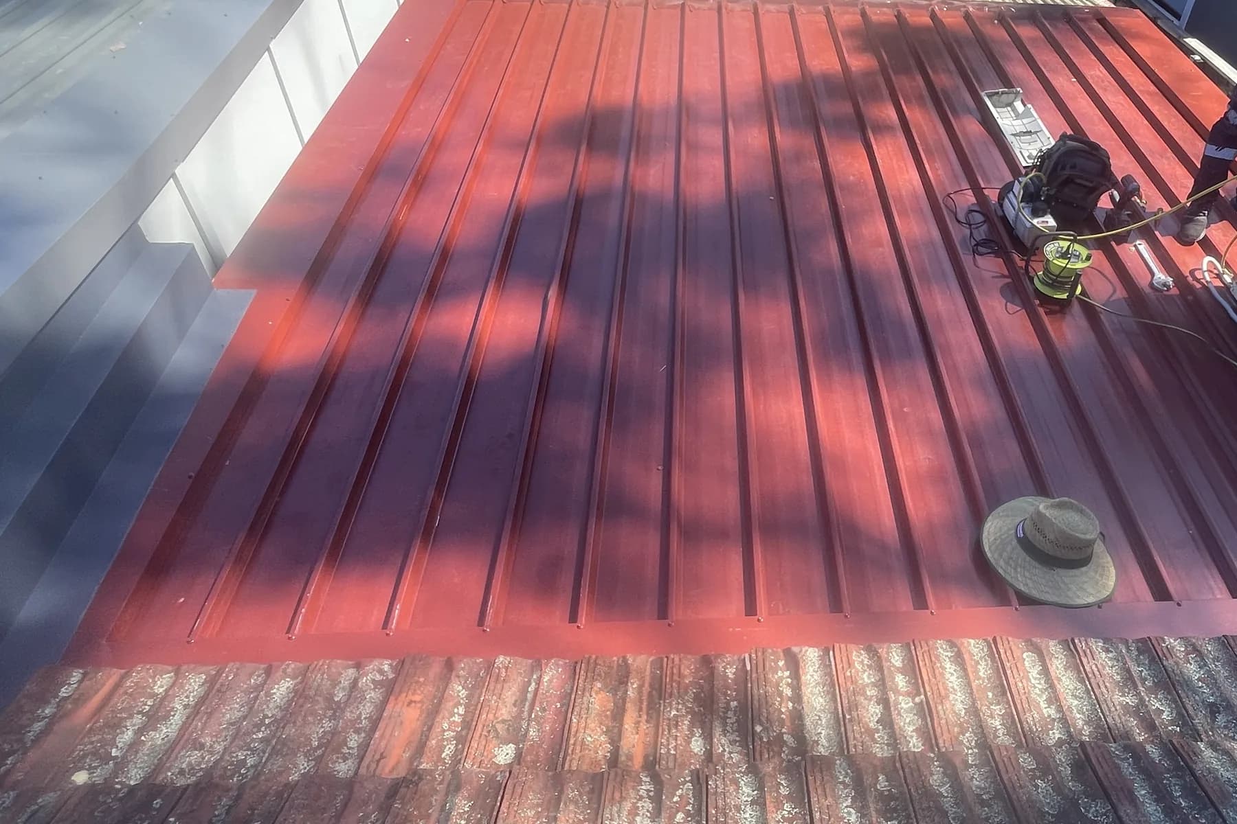 A roof part way through replacement, new red steel sheeting laid and the last of the old corrugated iron still at the edge