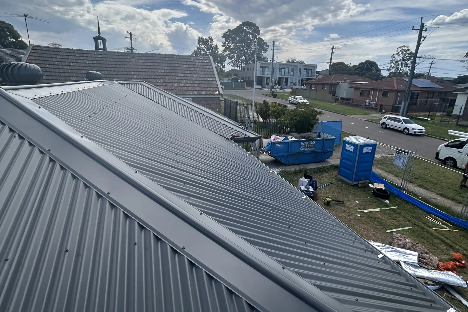 A hip roof part way through replacement, seen from the ridge out over a suburban street