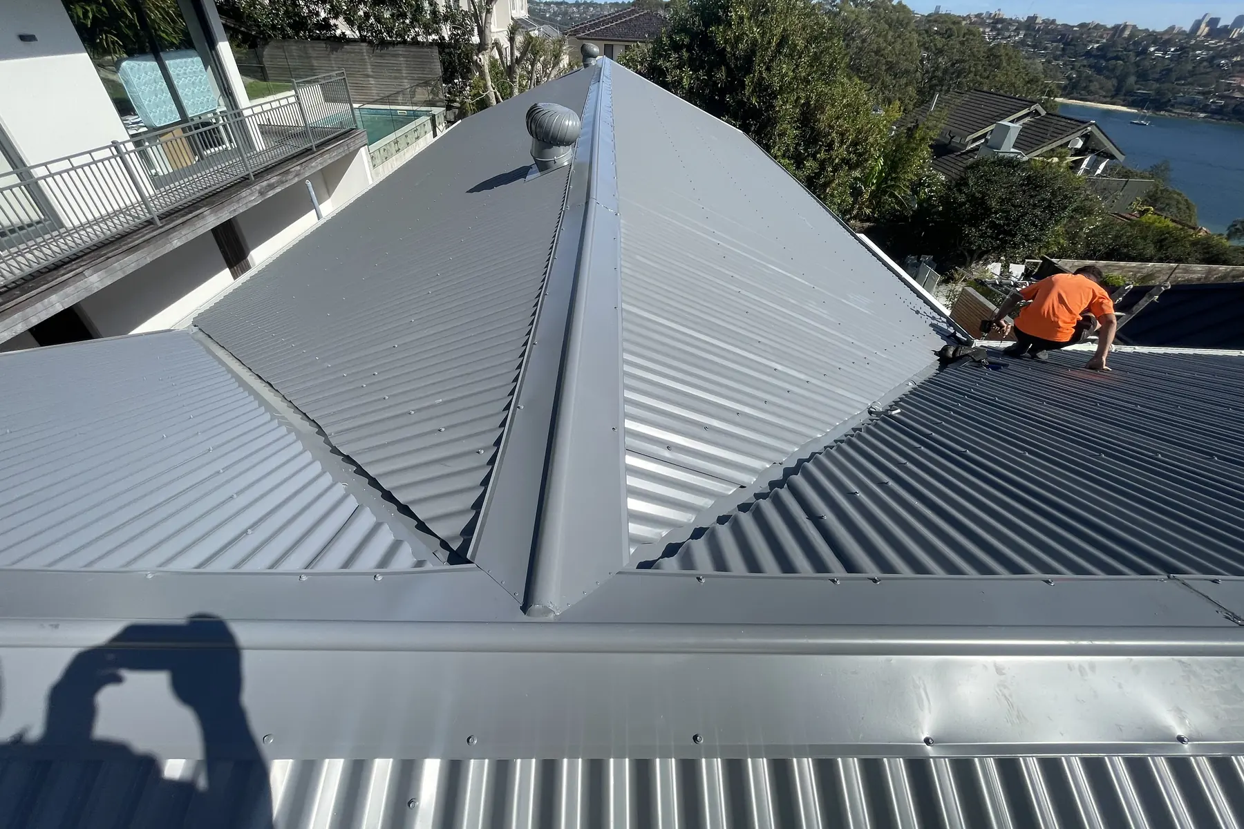 A roof plumber setting sheets along the hip of a new metal roof, water in the distance