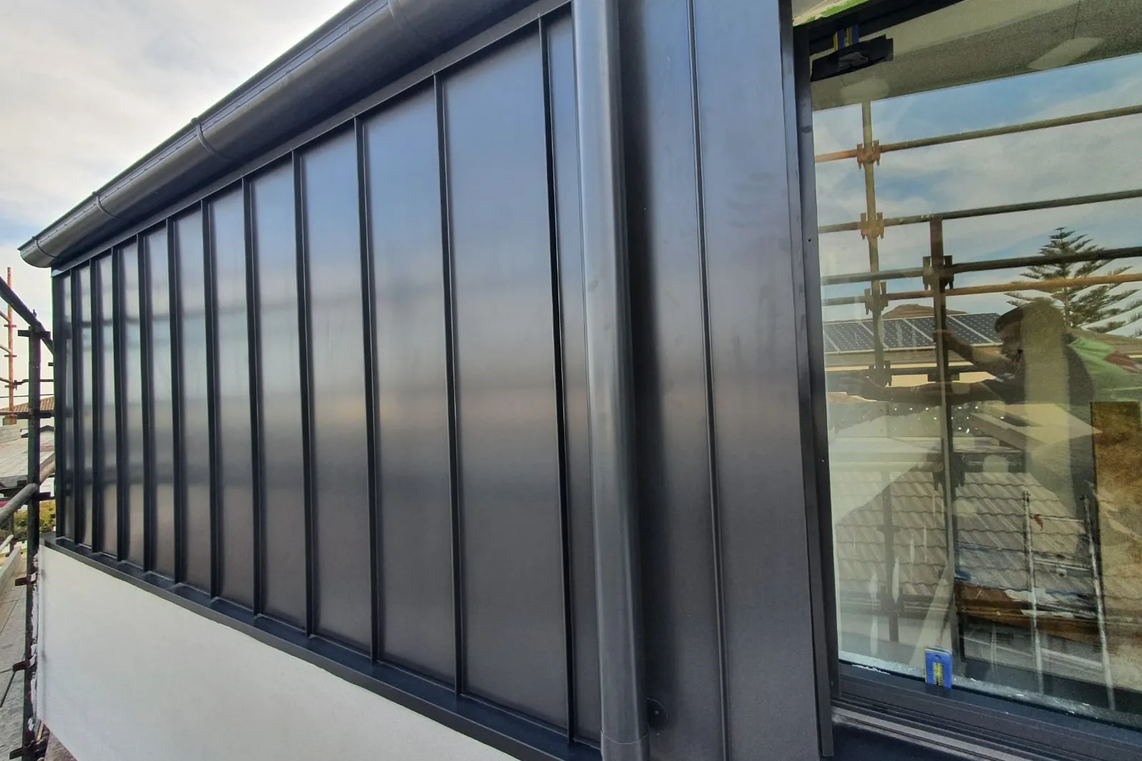 A dark standing seam elevation with the raised seams running vertically, glazing below and scaffold still up