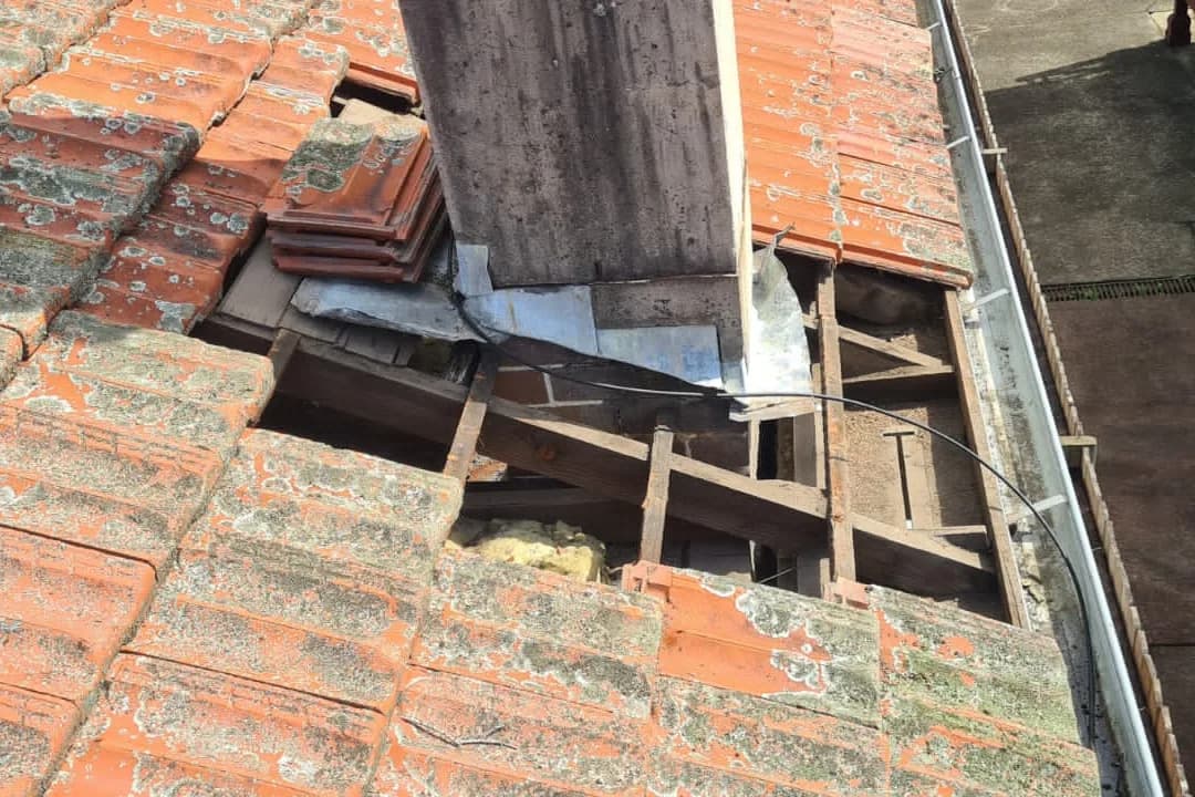 Old terracotta tiles lifted off a roof, exposing the battens and the perished flashing at a chimney