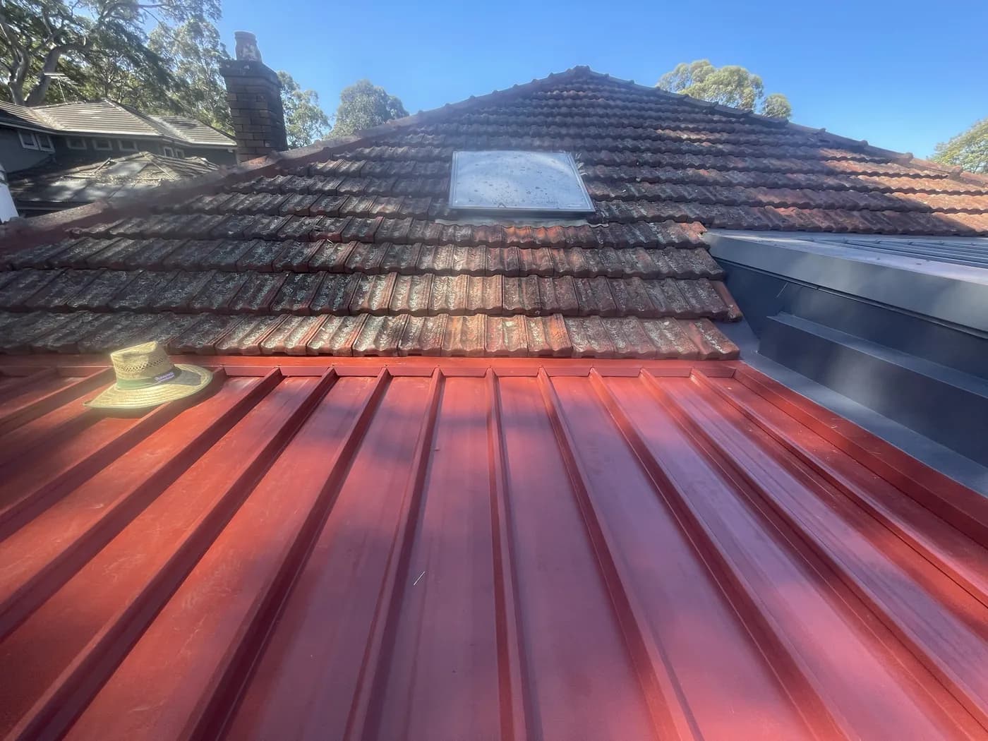 New red steel sheeting laid alongside the old terracotta tiles it is replacing, part way through the changeover